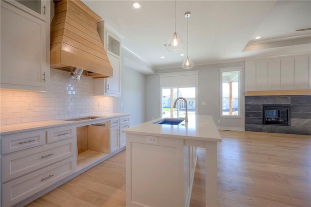 kitchen with sink, crown molding, white cabinetry, custom range hood, and a center island with sink