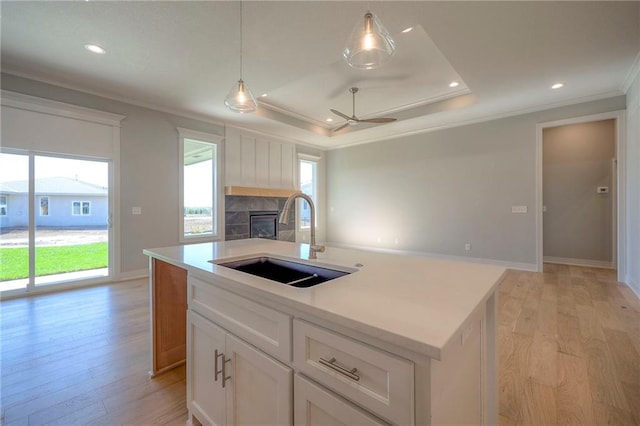 kitchen with white cabinetry, sink, hanging light fixtures, a tray ceiling, and a center island with sink