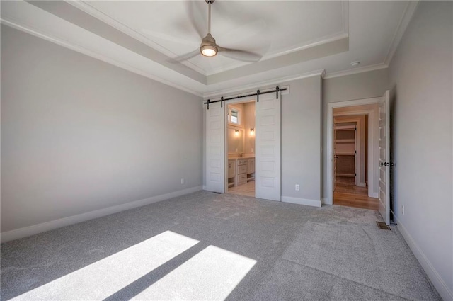 unfurnished bedroom with ensuite bath, ceiling fan, carpet flooring, a tray ceiling, and a barn door