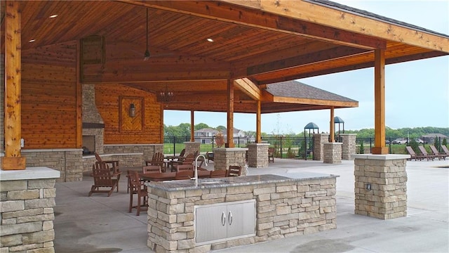 view of patio featuring a gazebo, exterior kitchen, a wet bar, and an outdoor stone fireplace