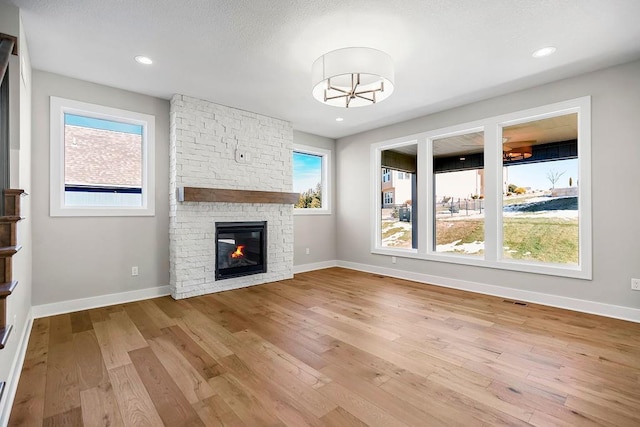 unfurnished living room with light wood finished floors, baseboards, visible vents, a stone fireplace, and recessed lighting