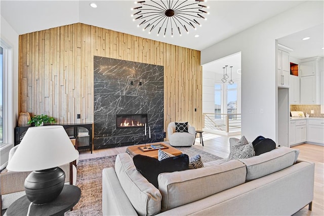 living room featuring a premium fireplace, wooden walls, light hardwood / wood-style floors, and lofted ceiling