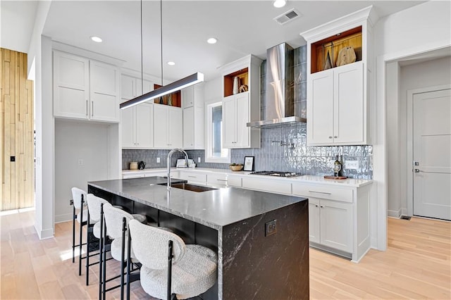 kitchen featuring tasteful backsplash, a kitchen island with sink, sink, wall chimney range hood, and white cabinets