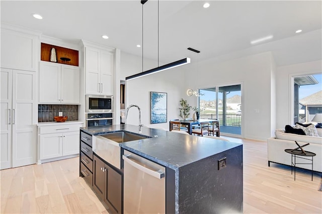 kitchen with white cabinets, decorative light fixtures, stainless steel appliances, and an island with sink