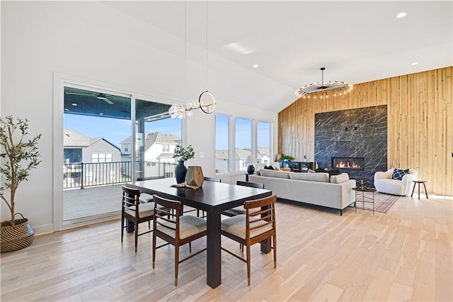 dining space with light wood-type flooring, an inviting chandelier, lofted ceiling, and wood walls