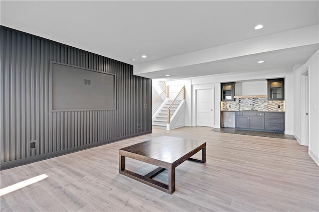 living room with light hardwood / wood-style floors, sink, and wooden walls