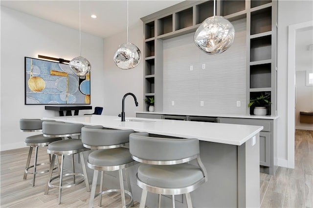 kitchen with gray cabinetry, decorative light fixtures, light wood-type flooring, and sink