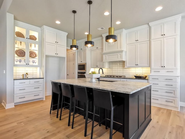 kitchen with white cabinetry, an island with sink, light stone counters, and built in microwave