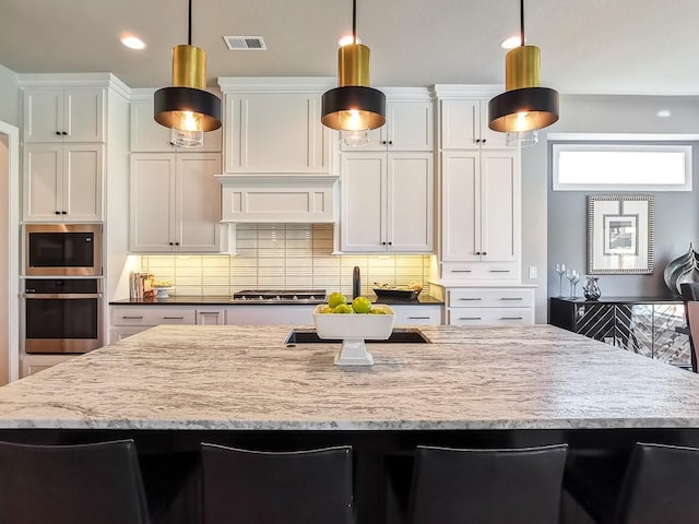 kitchen featuring appliances with stainless steel finishes, light stone countertops, hanging light fixtures, and white cabinets