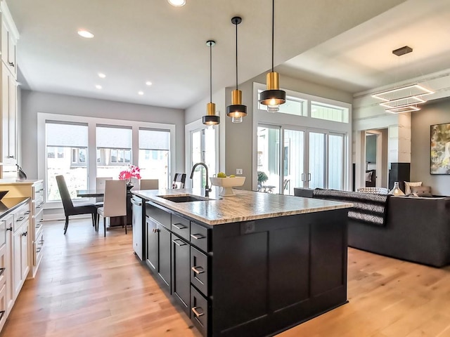 kitchen with french doors, sink, white cabinetry, hanging light fixtures, and an island with sink