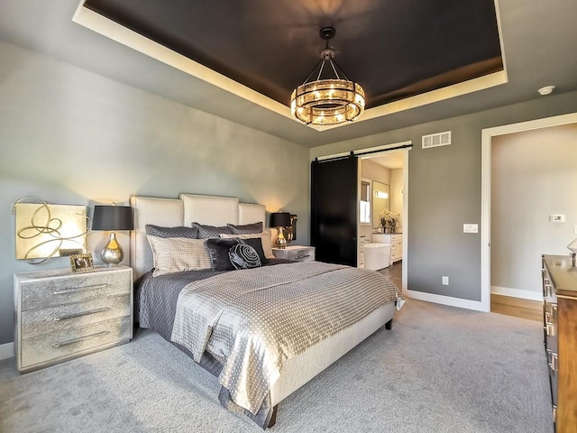 carpeted bedroom featuring ensuite bath, a tray ceiling, and a barn door