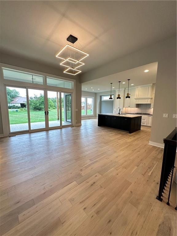 unfurnished living room featuring an inviting chandelier and light hardwood / wood-style flooring