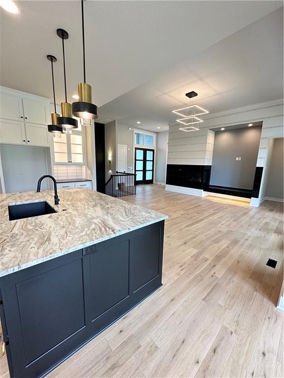 kitchen featuring light stone countertops, sink, pendant lighting, and white cabinets