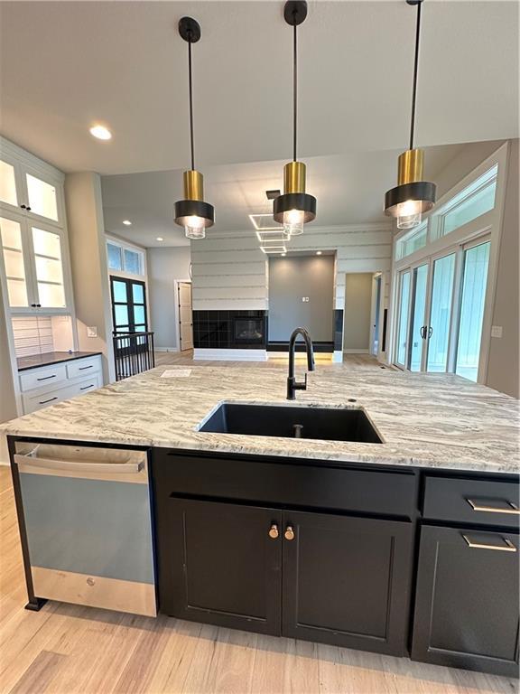 kitchen with hanging light fixtures, sink, stainless steel dishwasher, and light stone counters