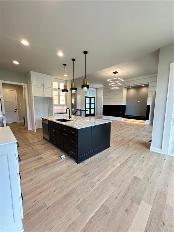 kitchen with sink, light hardwood / wood-style flooring, a kitchen island with sink, hanging light fixtures, and white cabinets