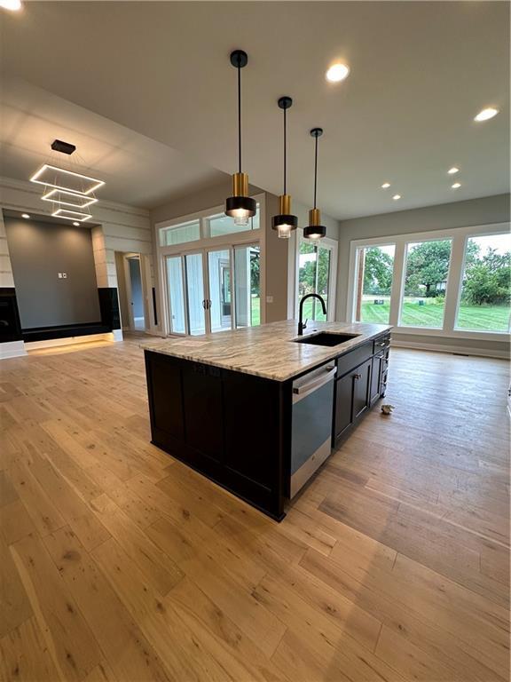 kitchen with sink, dishwasher, hanging light fixtures, light stone counters, and light hardwood / wood-style floors