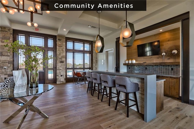 bar featuring coffered ceiling, a breakfast bar, hardwood / wood-style flooring, pendant lighting, and beam ceiling