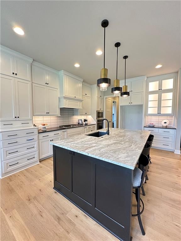 kitchen with pendant lighting, sink, a large island, white cabinetry, and light stone countertops