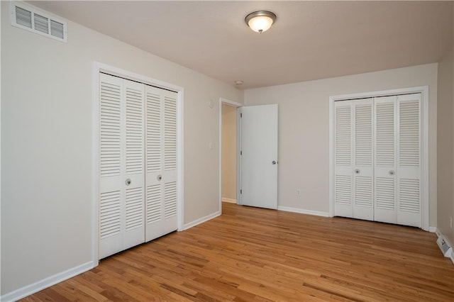 unfurnished bedroom with two closets and light wood-type flooring