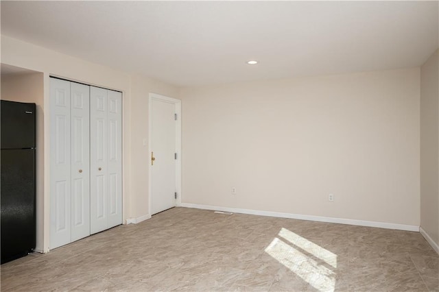 unfurnished bedroom featuring light tile floors and black fridge