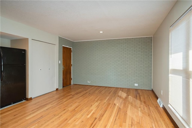 unfurnished bedroom with brick wall, light wood-type flooring, and black refrigerator