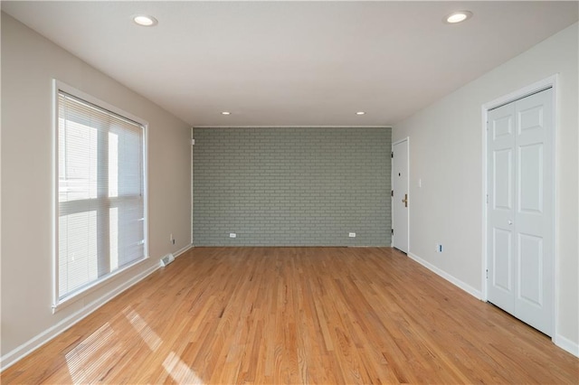 empty room with light hardwood / wood-style flooring, brick wall, and a healthy amount of sunlight