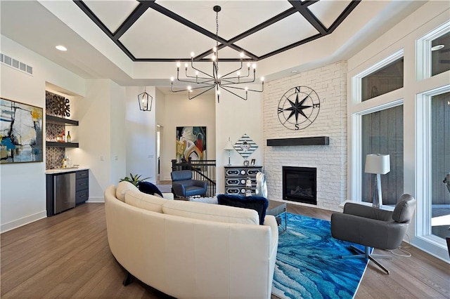 living room with coffered ceiling, a notable chandelier, a fireplace, brick wall, and dark wood-type flooring