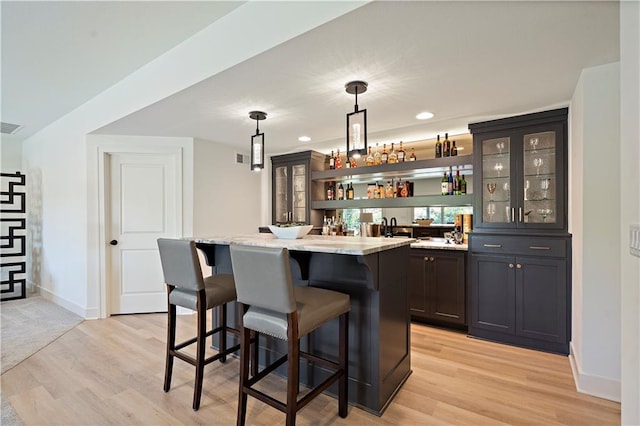 bar with light wood-type flooring, light stone countertops, and pendant lighting