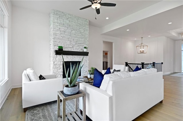 living room featuring ceiling fan with notable chandelier, light wood-type flooring, a wealth of natural light, and a fireplace