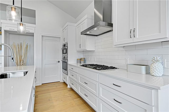 kitchen with white cabinetry, hanging light fixtures, sink, appliances with stainless steel finishes, and wall chimney exhaust hood