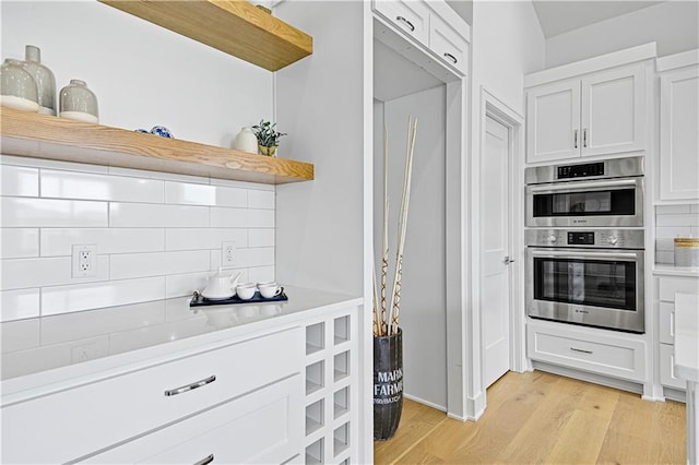 kitchen with white cabinetry, stainless steel double oven, decorative backsplash, and light hardwood / wood-style flooring