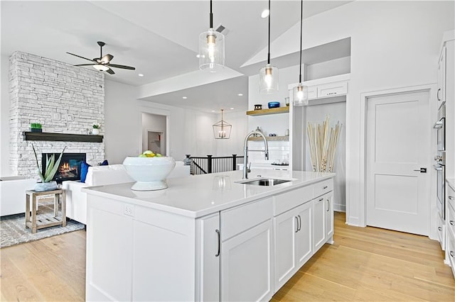 kitchen with light hardwood / wood-style flooring, an island with sink, pendant lighting, sink, and white cabinetry