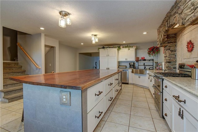 kitchen featuring white cabinetry, wood counters, a spacious island, a textured ceiling, and appliances with stainless steel finishes