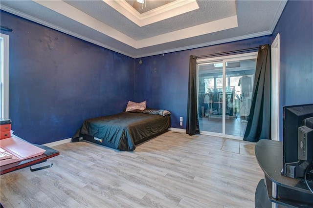 bedroom with access to exterior, light hardwood / wood-style floors, a raised ceiling, and ornamental molding