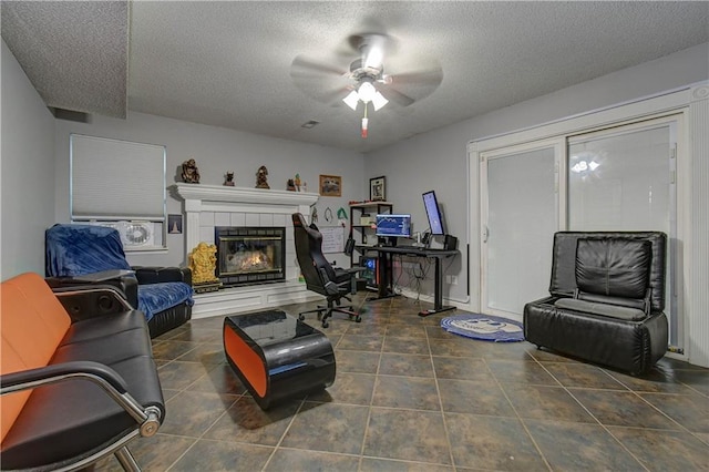 tiled living room featuring ceiling fan, a textured ceiling, and a tiled fireplace