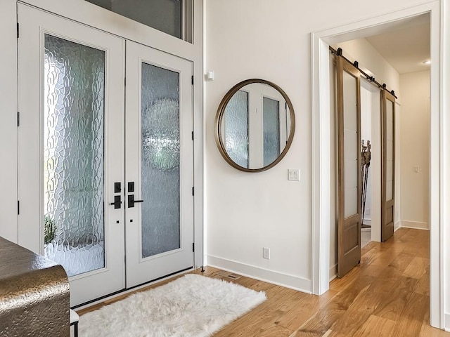 doorway with a barn door, french doors, and light wood-type flooring