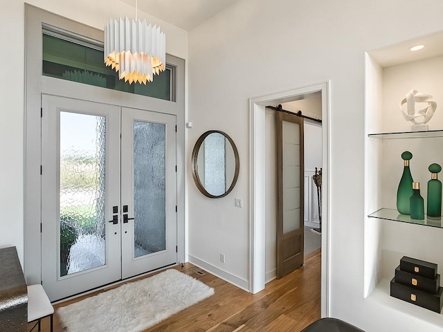 entrance foyer with a chandelier, french doors, a barn door, and wood-type flooring