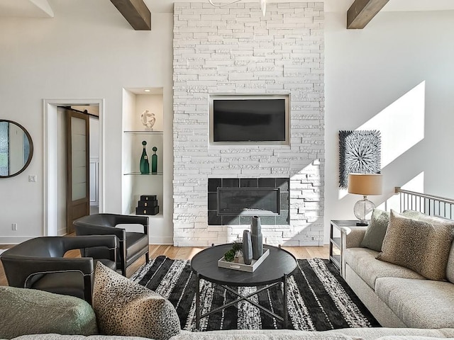 living room featuring beam ceiling, a stone fireplace, and wood-type flooring