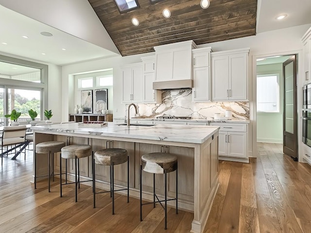 kitchen featuring white cabinets, a kitchen bar, a center island with sink, and sink