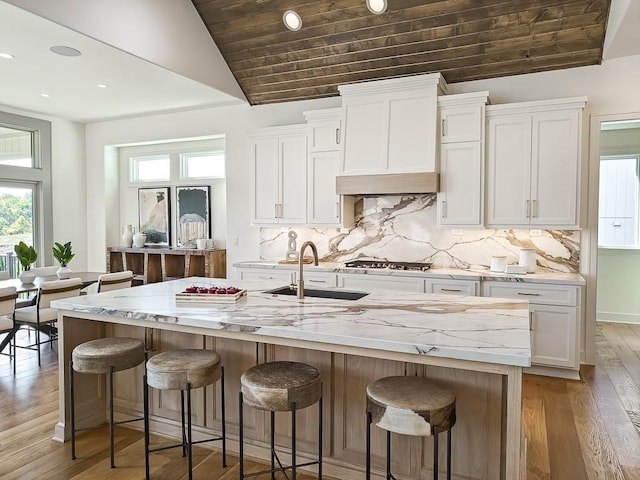 kitchen featuring sink, an island with sink, lofted ceiling, white cabinets, and custom range hood