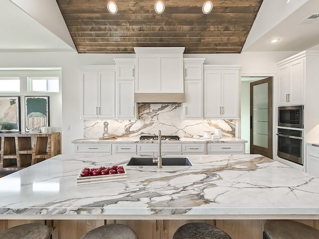 kitchen with appliances with stainless steel finishes, white cabinetry, lofted ceiling, and a large island