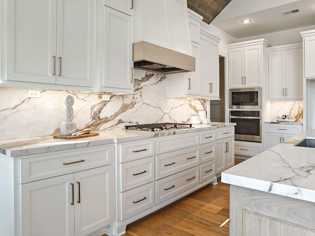 kitchen with decorative backsplash, light wood-type flooring, appliances with stainless steel finishes, light stone counters, and white cabinetry