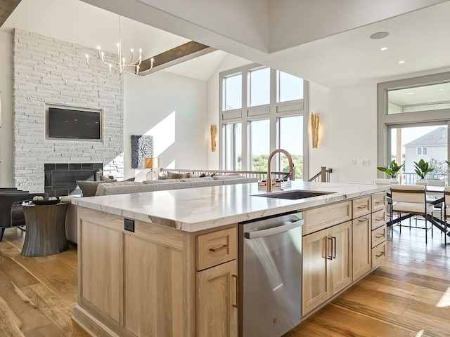 kitchen with light brown cabinets, sink, stainless steel dishwasher, light wood-type flooring, and an island with sink