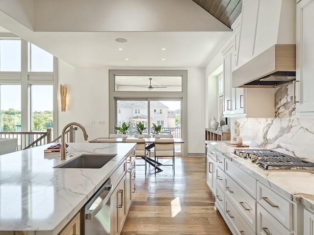 kitchen with light stone countertops, sink, decorative backsplash, white cabinets, and custom exhaust hood