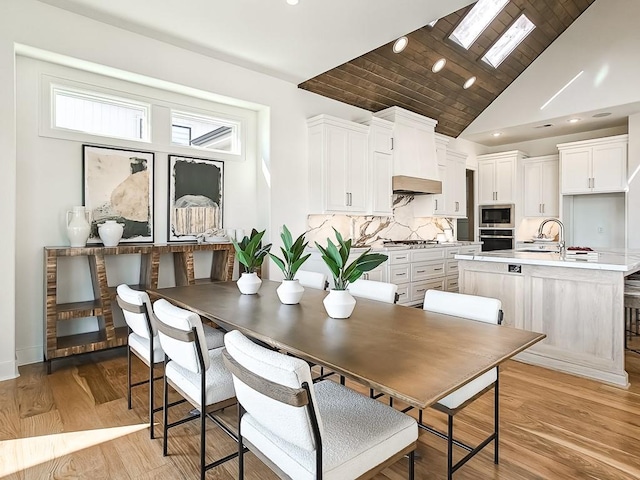 dining area with a skylight, light hardwood / wood-style flooring, high vaulted ceiling, and sink