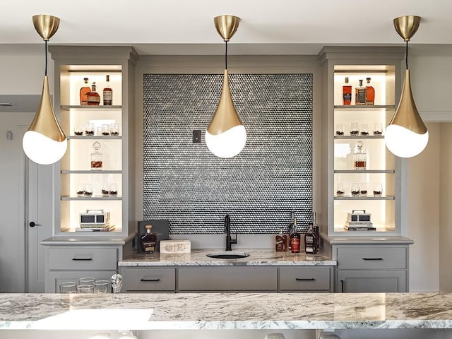 bar featuring gray cabinetry, light stone countertops, sink, and hanging light fixtures