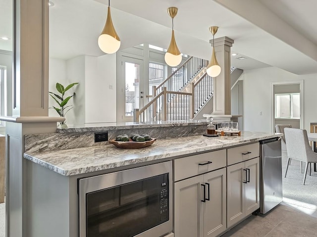 kitchen with hanging light fixtures, gray cabinets, light stone counters, and stainless steel microwave