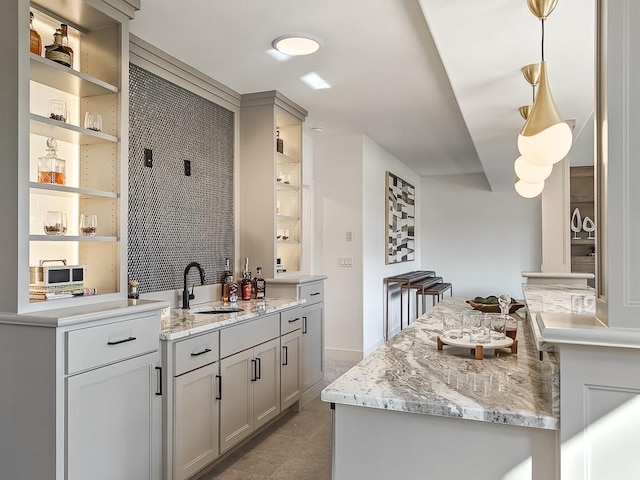 bar featuring light stone countertops, sink, and decorative light fixtures