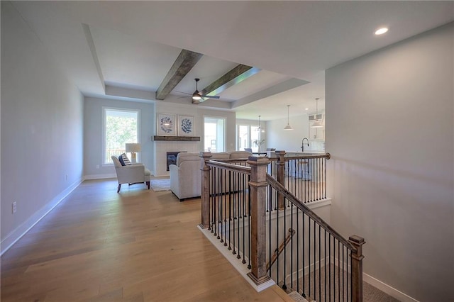 stairs with baseboards, beamed ceiling, a tile fireplace, wood finished floors, and a ceiling fan