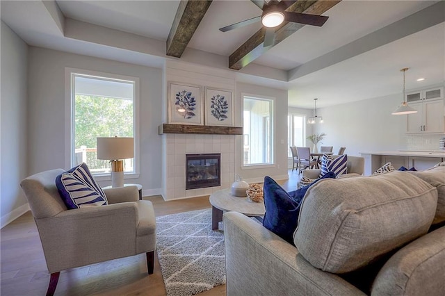 living area featuring beam ceiling, light wood-style floors, baseboards, and ceiling fan